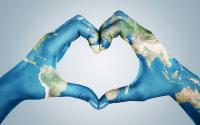 Female hands, painted in the world map,  forming heart shape isolated on blue background